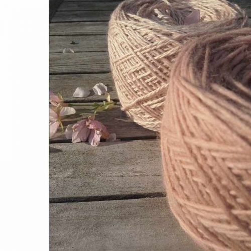 2 altrosa gefärbte Wollknäuel auf Holztisch mit rosa Blüte