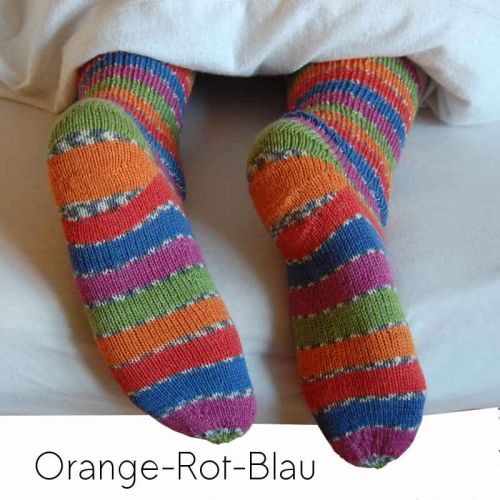 Bunte Ringelsocken auf Füßen, die unter Decke hervorschauen