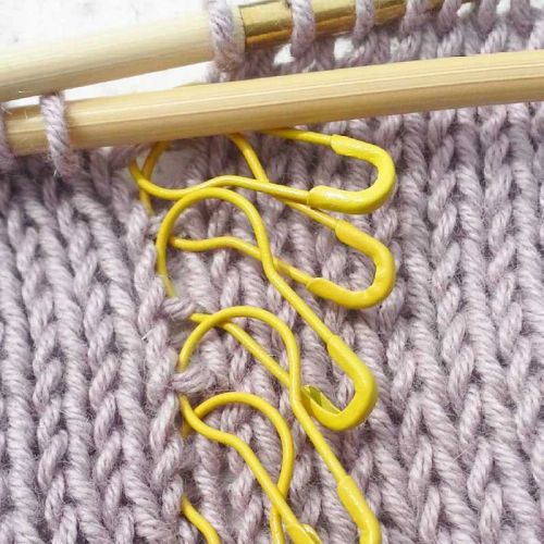 Gelbe Maschenmarkierer auf Strickstück in flieder